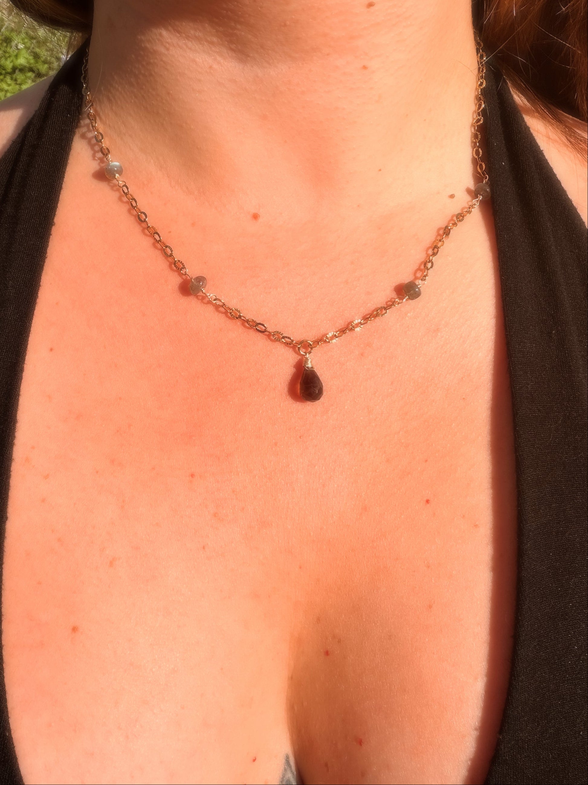 Close-up of a smoky quartz and labradorite stainless steel gold necklace with a teardrop pendant on a person wearing a black top.