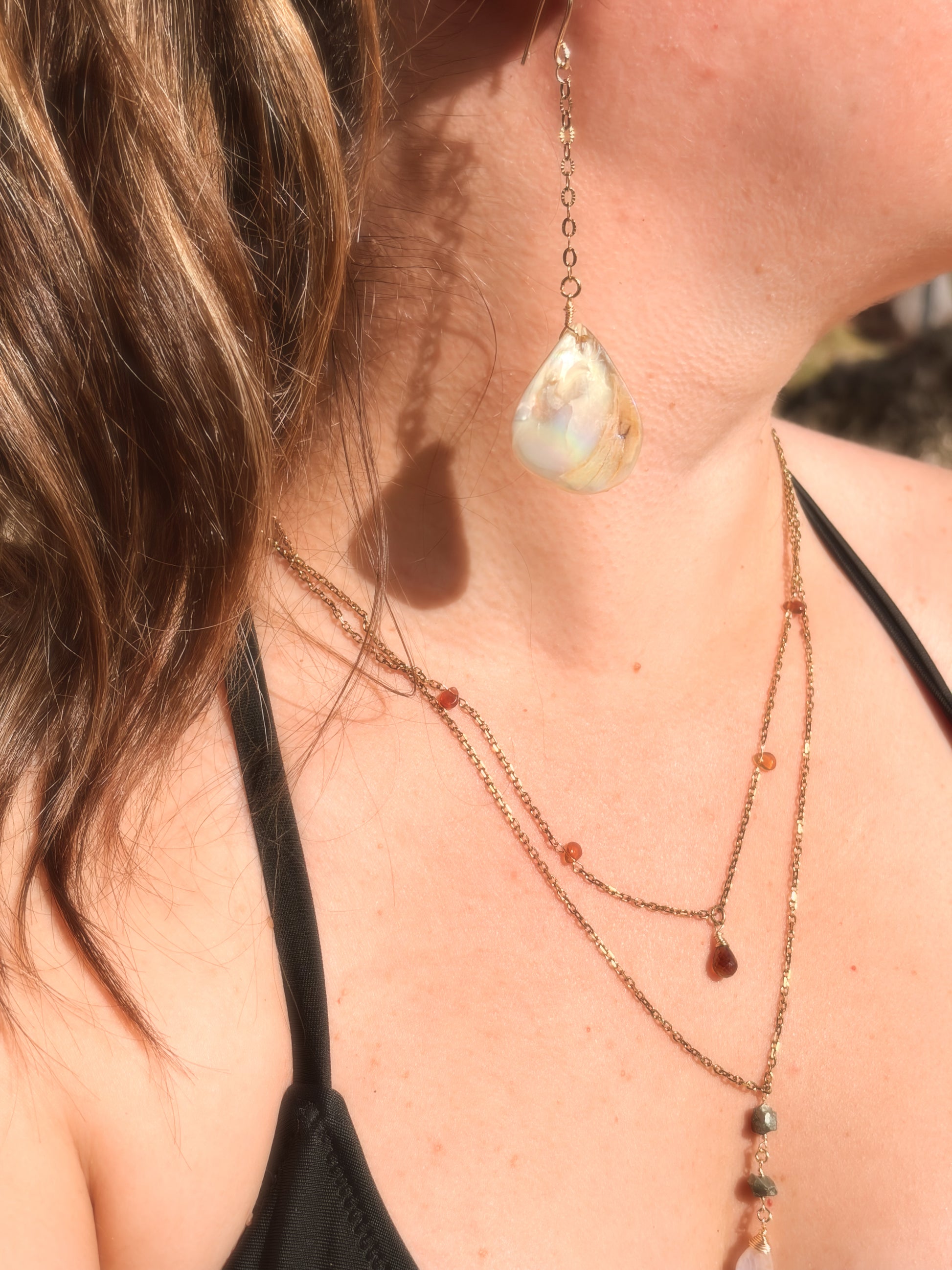 Close-up of a woman wearing layered stainless steel and crystal necklaces and  gold pearl earring.