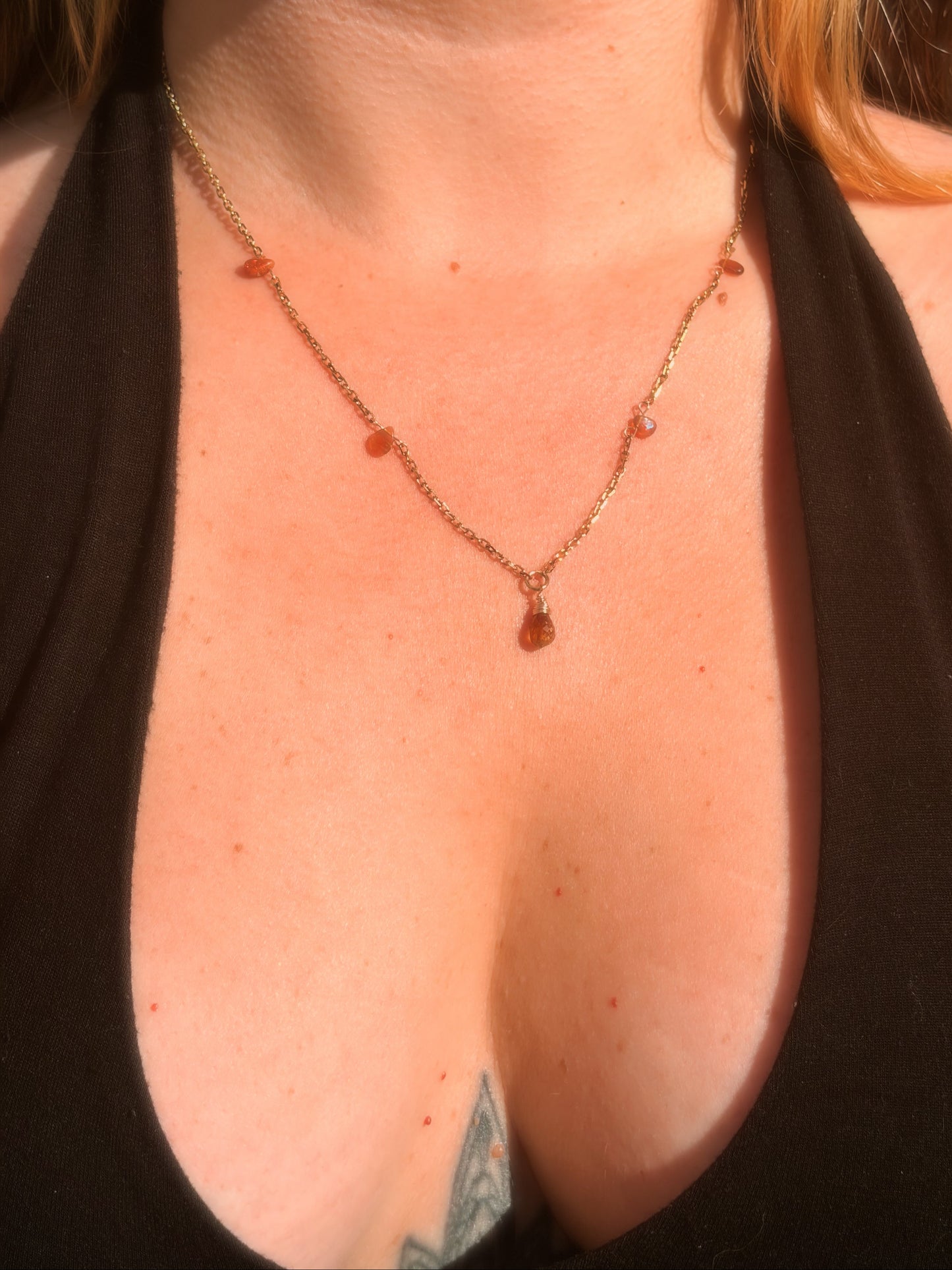 Close-up of a stainless steel gold necklace with amber-colored Tundra Tourmaline and Ethiopian Opal beads on a person wearing a black top.