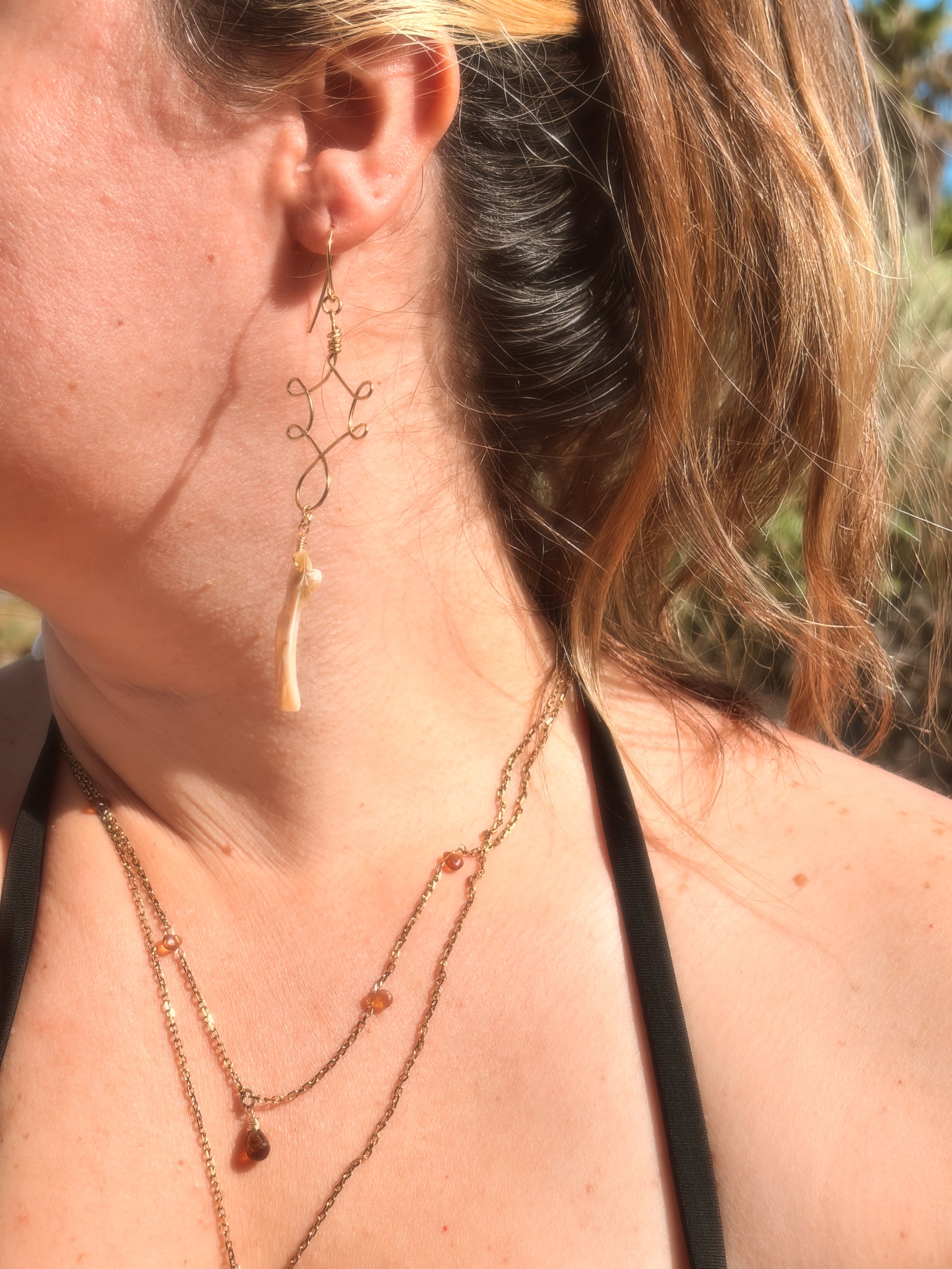 Close-up of a person wearing wire wrapped stainless steel gold brass earrings with an abalone shell bead and layered necklaces with a blurred background
