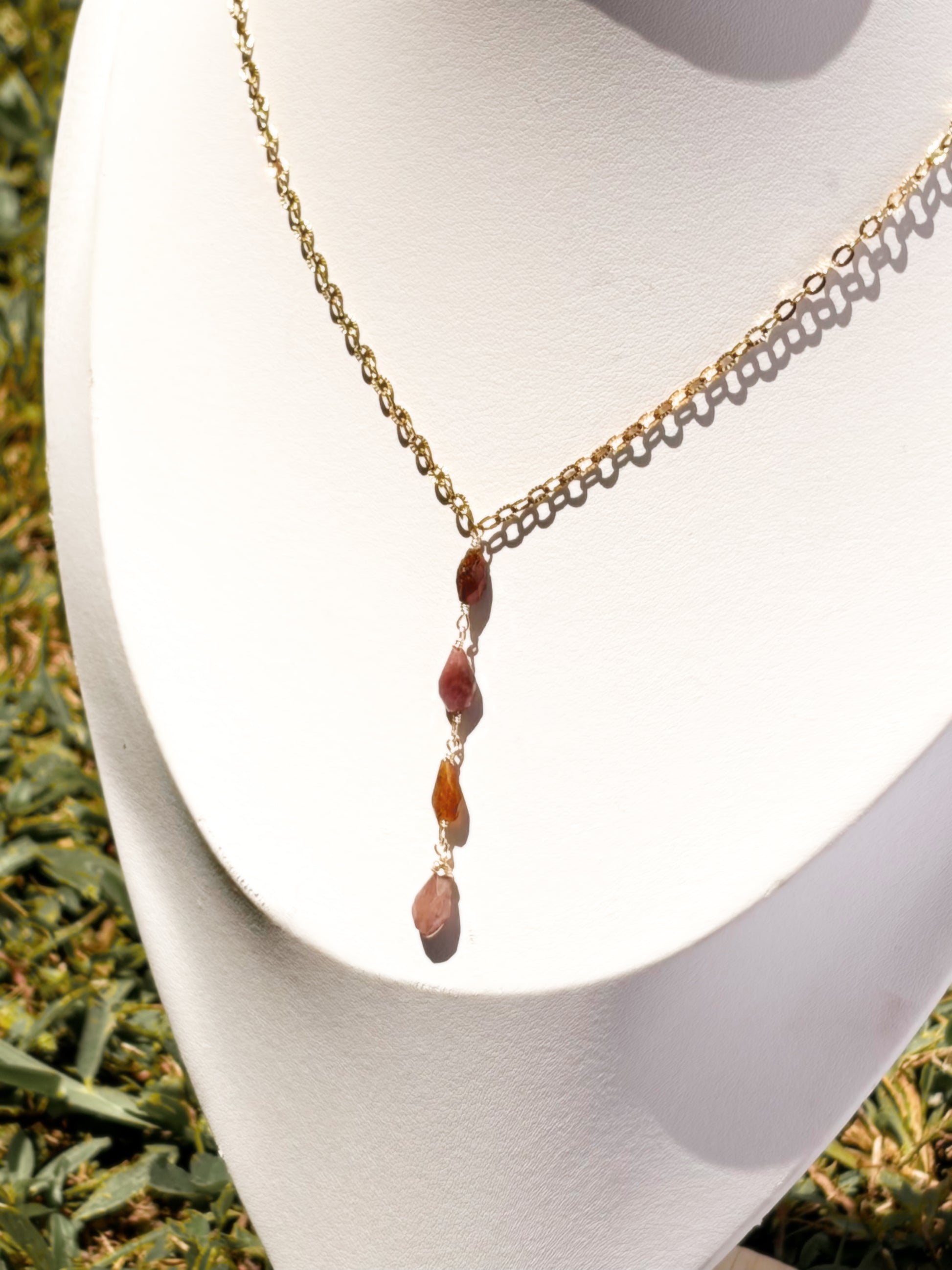 A gold chain necklace, lariat style necklace with pink and orange tourmaline stone beads, displayed on a white jewelry bust.