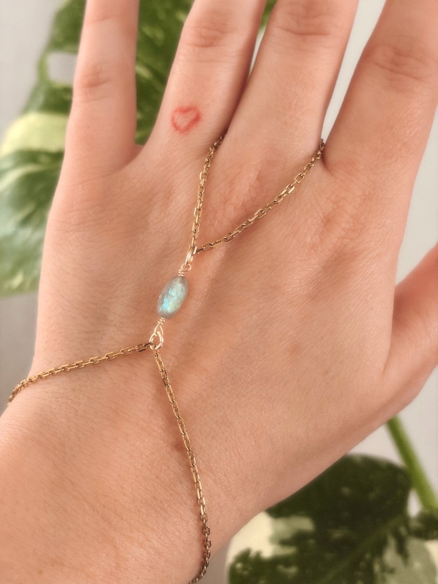 Gold stainless steel handchain bracelet with Labradorite beads on a person's wrist against a neutral background.