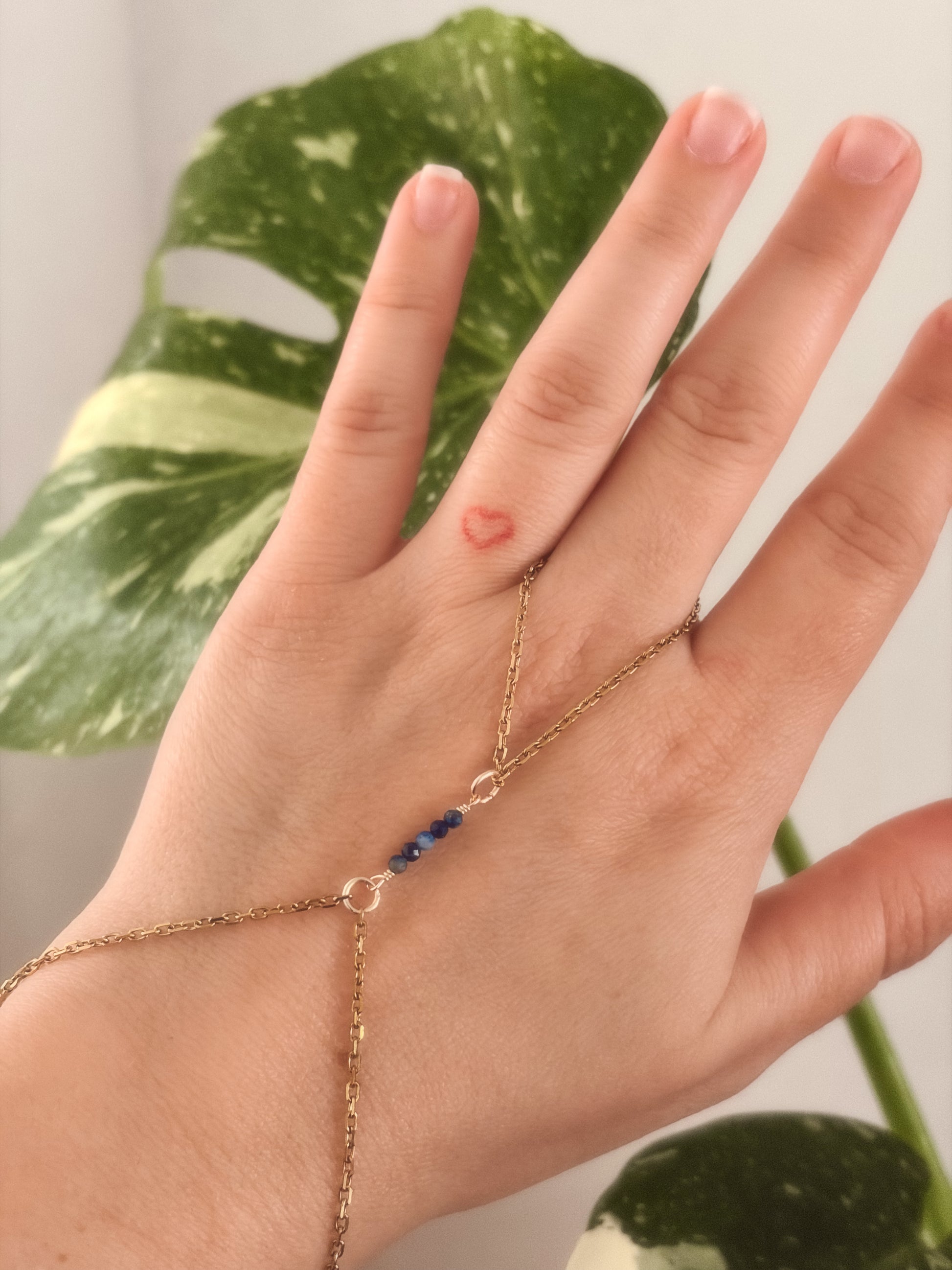Gold Stainless Steel tarnish resistant handchain with blue Sodalite beads on a person's hand against a blurred background with a monsterra plant. 