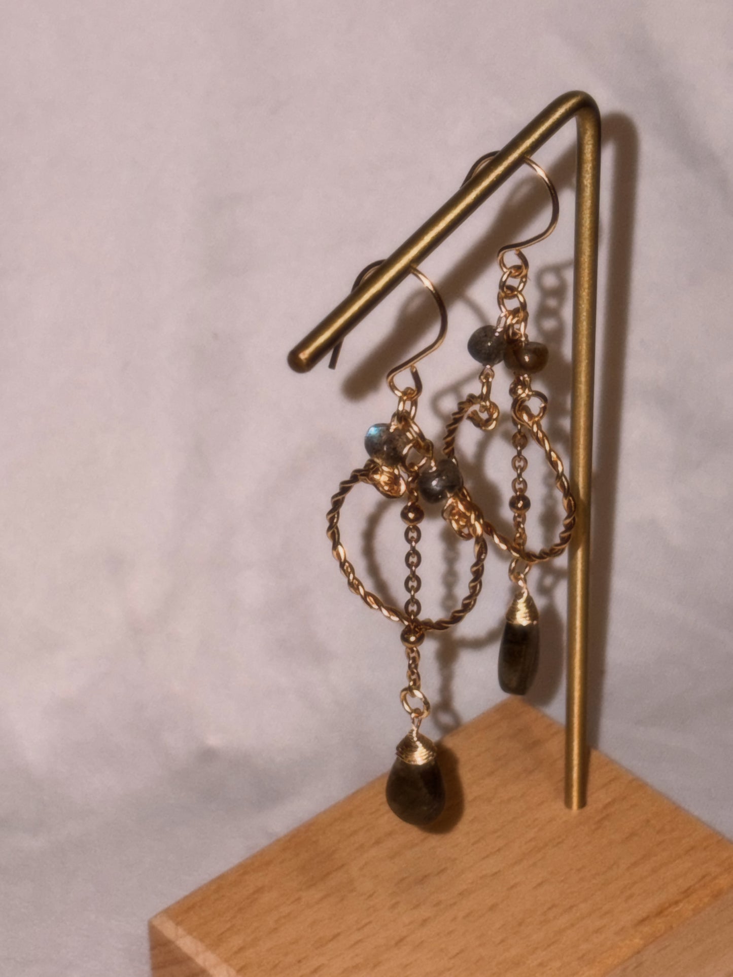 Gold brass and stainless steel hoop earrings with small and teardrop shaped Labradorite beads on a gold stand against a light background. 