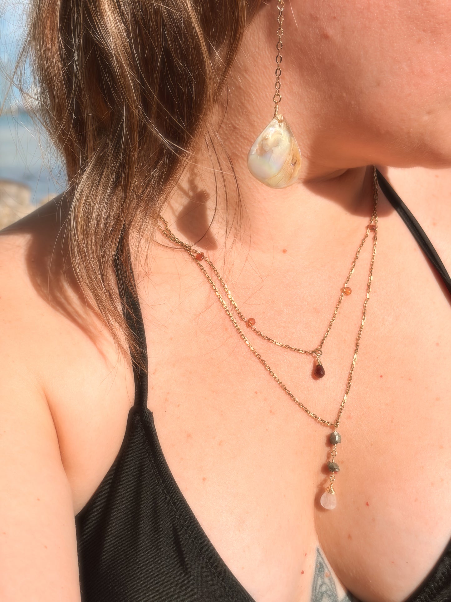 Close-up of a woman wearing layered stainless steel and crystal necklaces and  gold pearl earring.