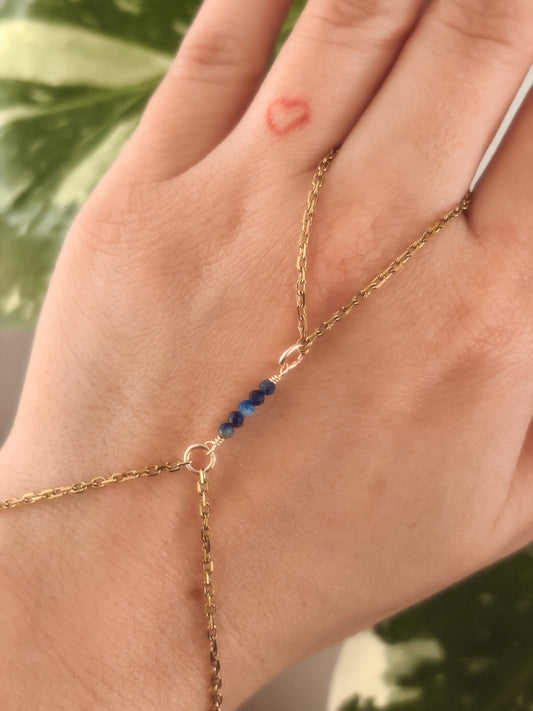 Gold Stainless Steel tarnish resistant handchain with blue Sodalite beads on a person's hand against a blurred background with a monsterra plant. 