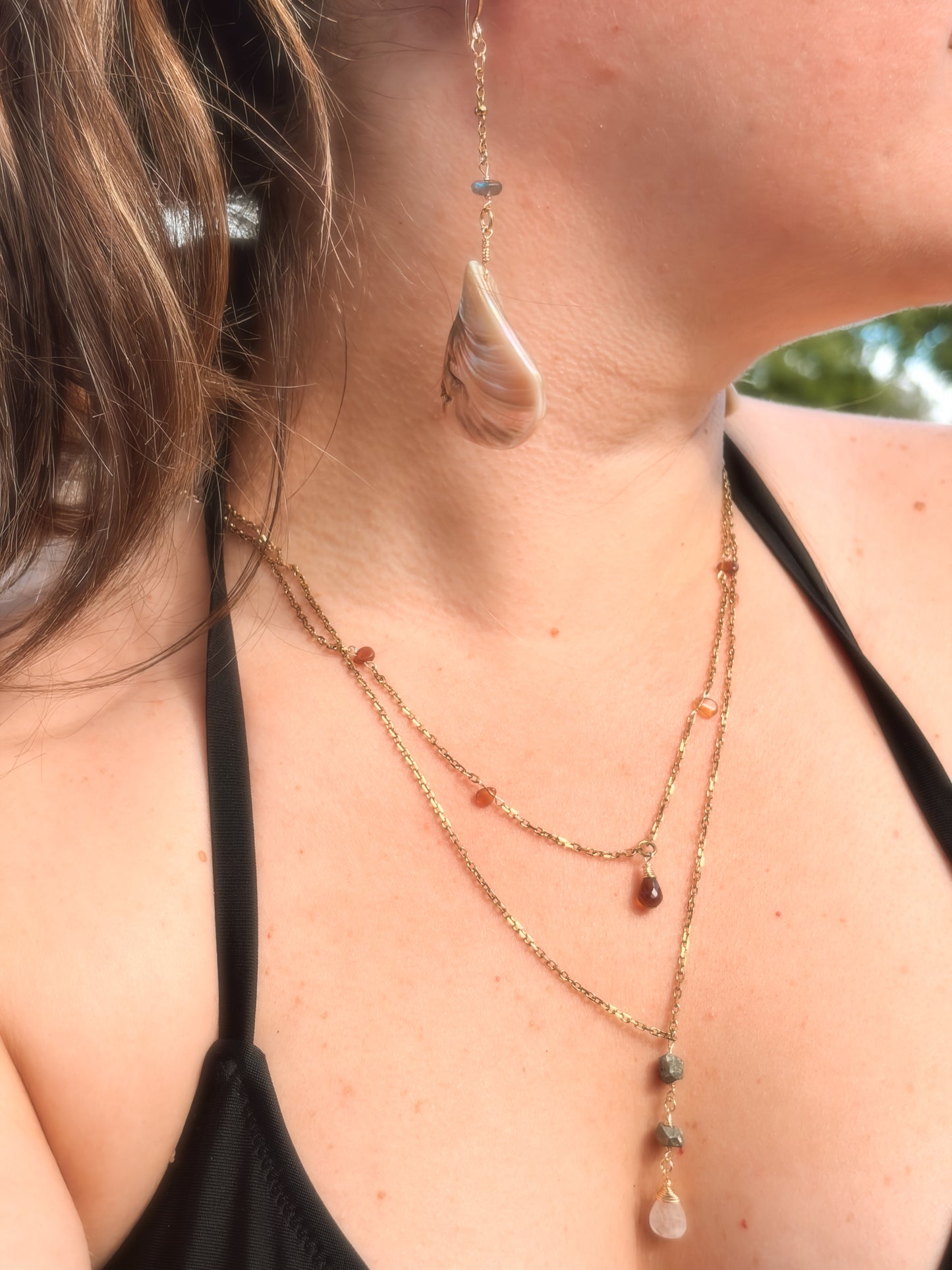 Person wearing layered crystal necklaces and Stainless Steel Gold dangly shell earrings with labradorite bead crystal.