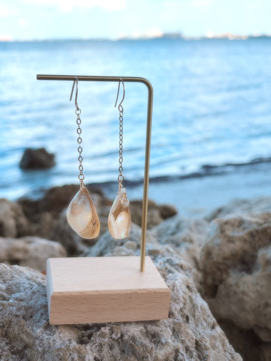 Beach close up of stainless steel dangly gold pearl/shell earrings.