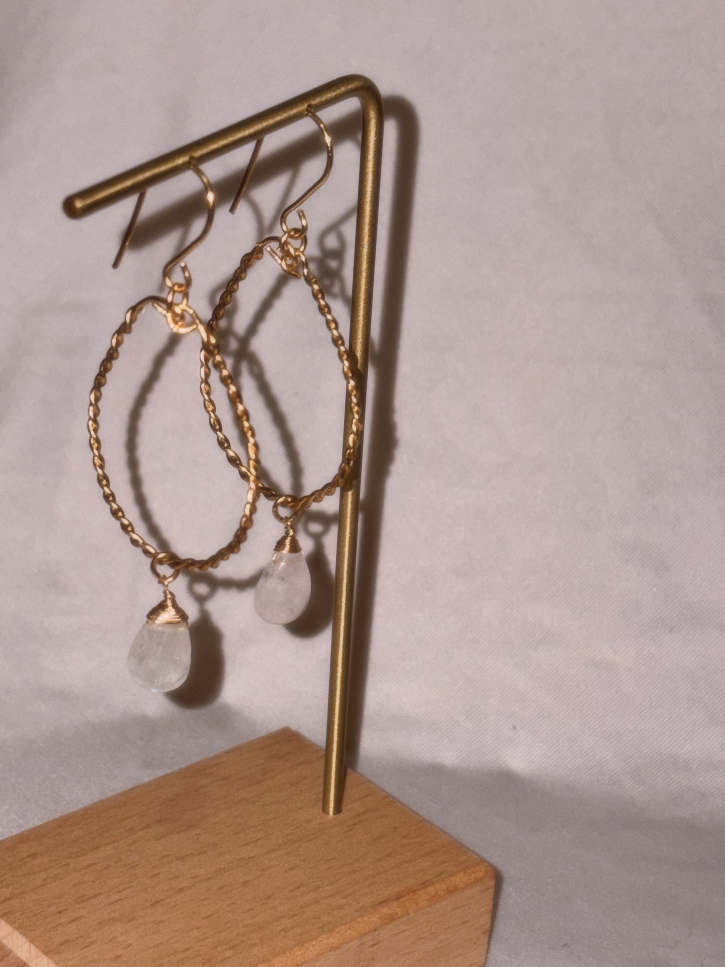 Gold hoop earrings with clear Rainbow Moonstone stones on a light background.