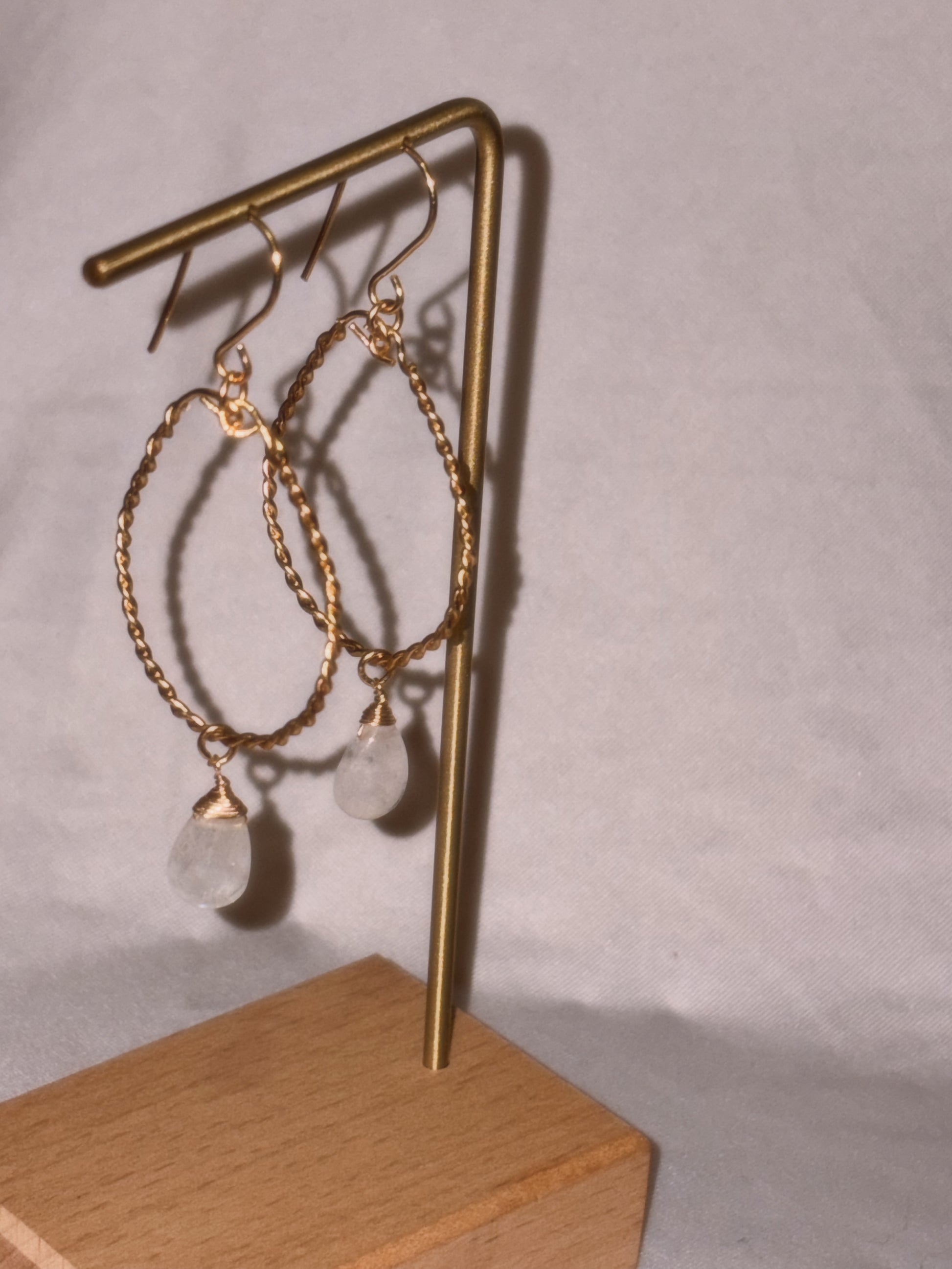Gold hoop earrings with clear Rainbow Moonstone stones on a light background.