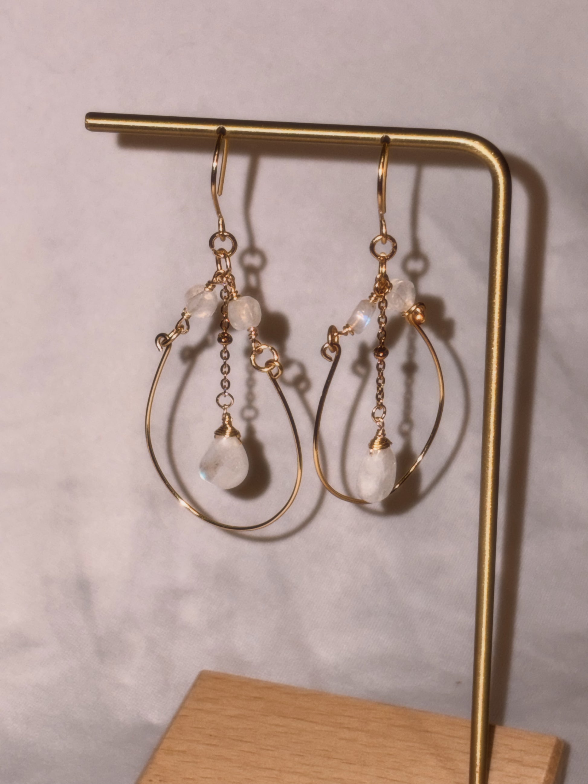Gold brass and stainless steel hoop earrings with small Rainbow Moonstone beads on a gold stand against a light background. 
