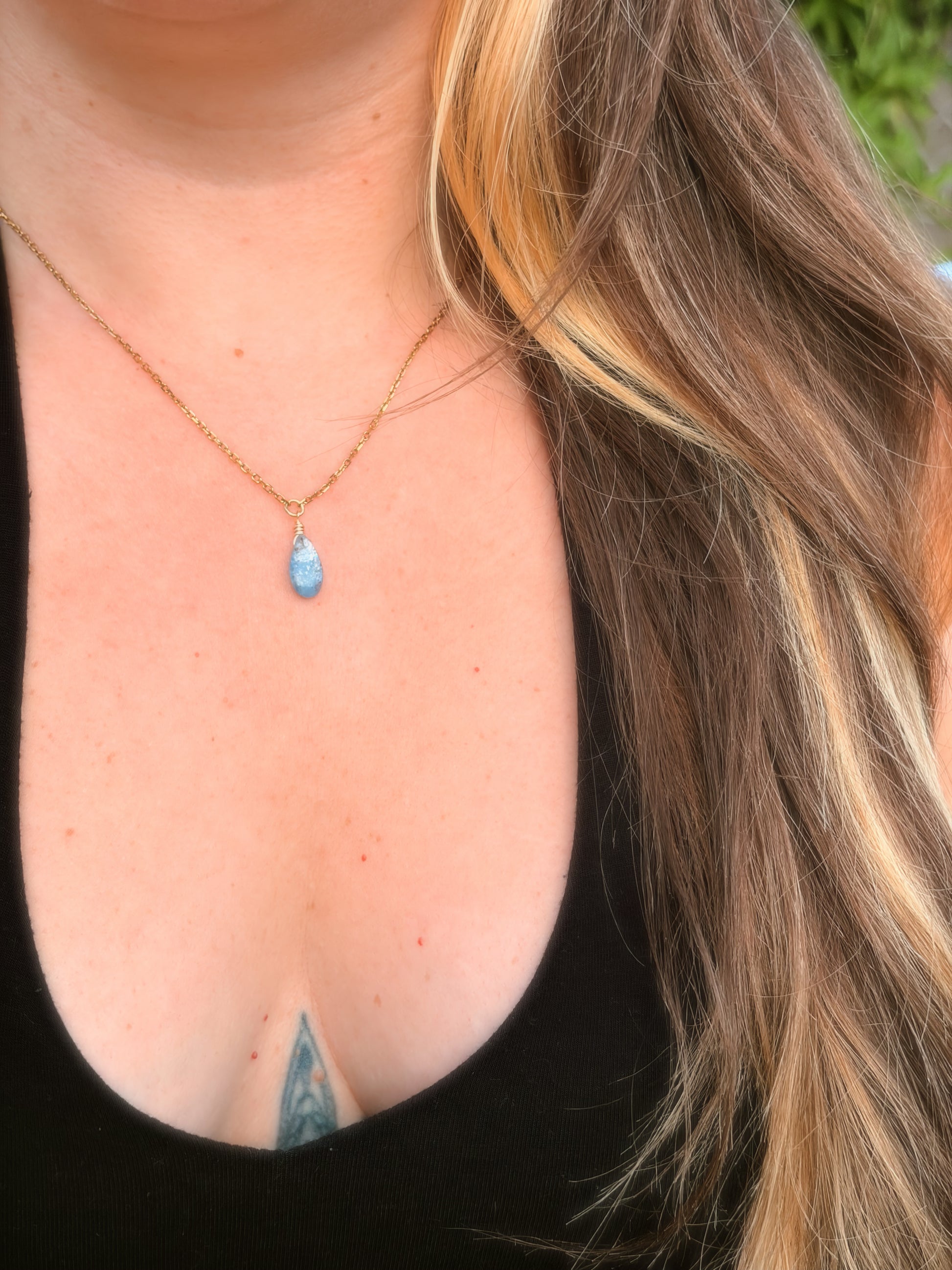 Gold Stainless Steel Necklace holding a Blue Kyanite gemstone on somone's neck with a black top.