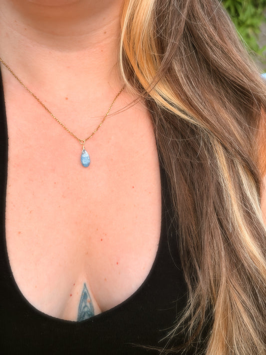 Gold Stainless Steel Necklace holding a Blue Kyanite gemstone on somone's neck with a black top.