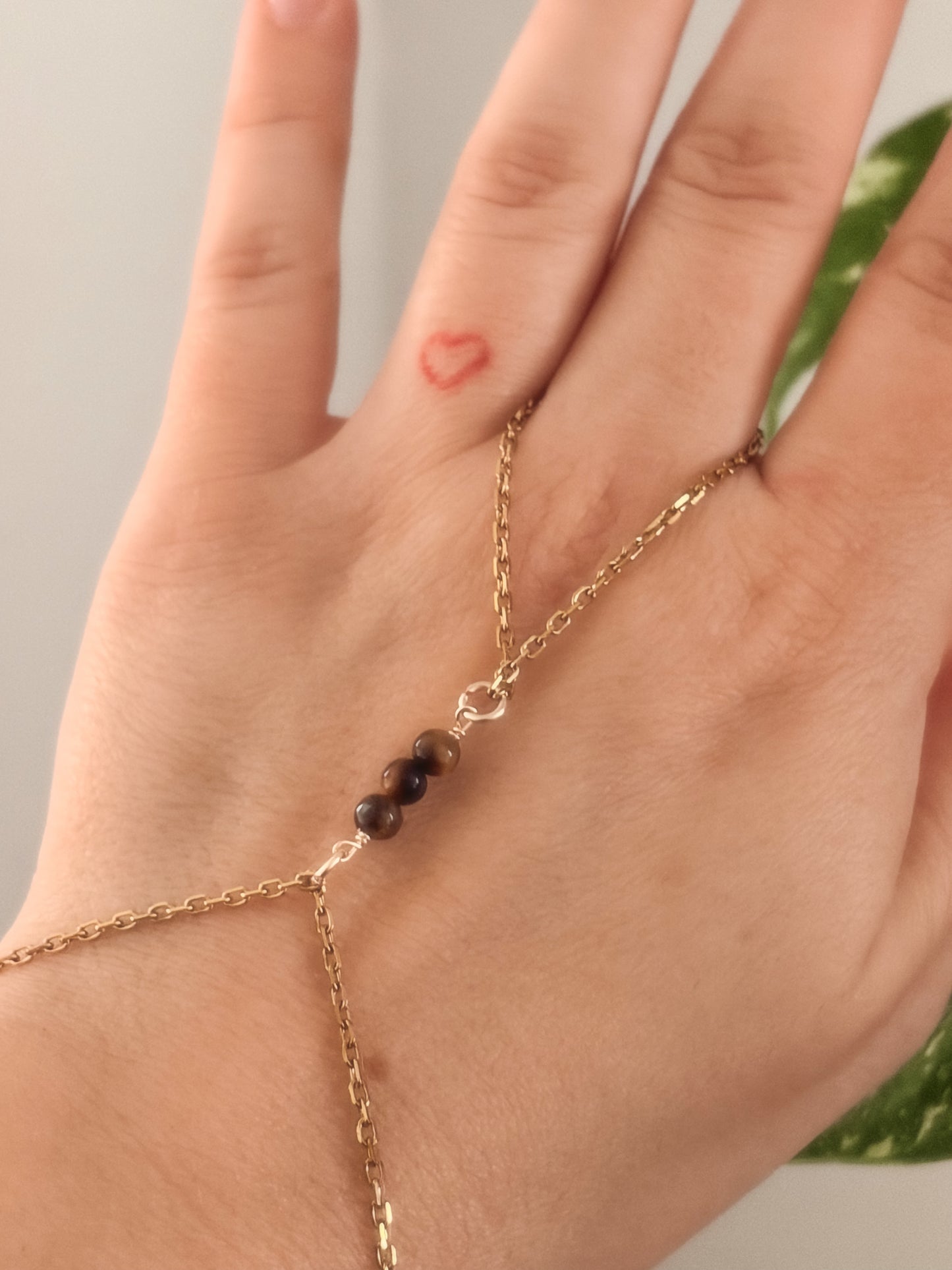 Gold stainless steel handchain bracelet with Tiger Eye beads on a person's wrist against a neutral background.