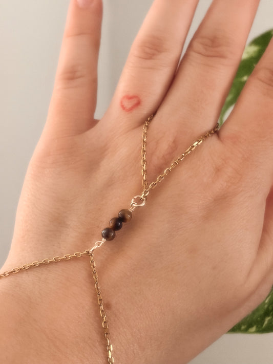 Gold stainless steel handchain bracelet with Tiger Eye beads on a person's wrist against a neutral background.