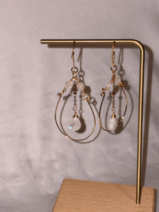 Gold brass and stainless steel hoop earrings with small Rainbow Moonstone beads on a gold stand against a light background. 