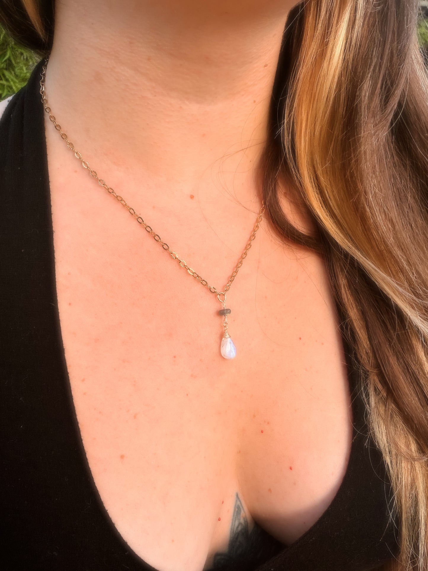 Close-up of a rainbow moonstone and labradorite stainless steel gold necklace with a teardrop pendant on a person wearing a black top.