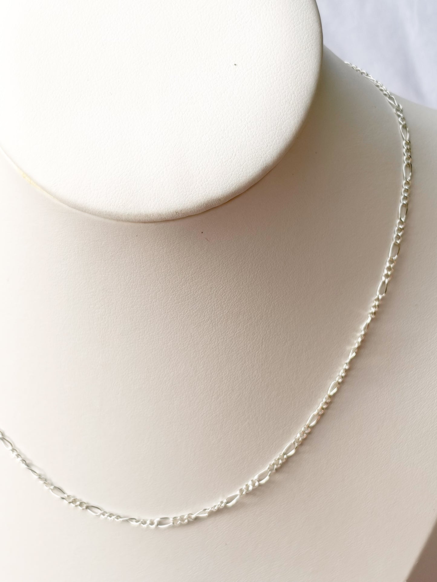Close up of Figaro Silver chain Necklace on a white mannequin bust and background.