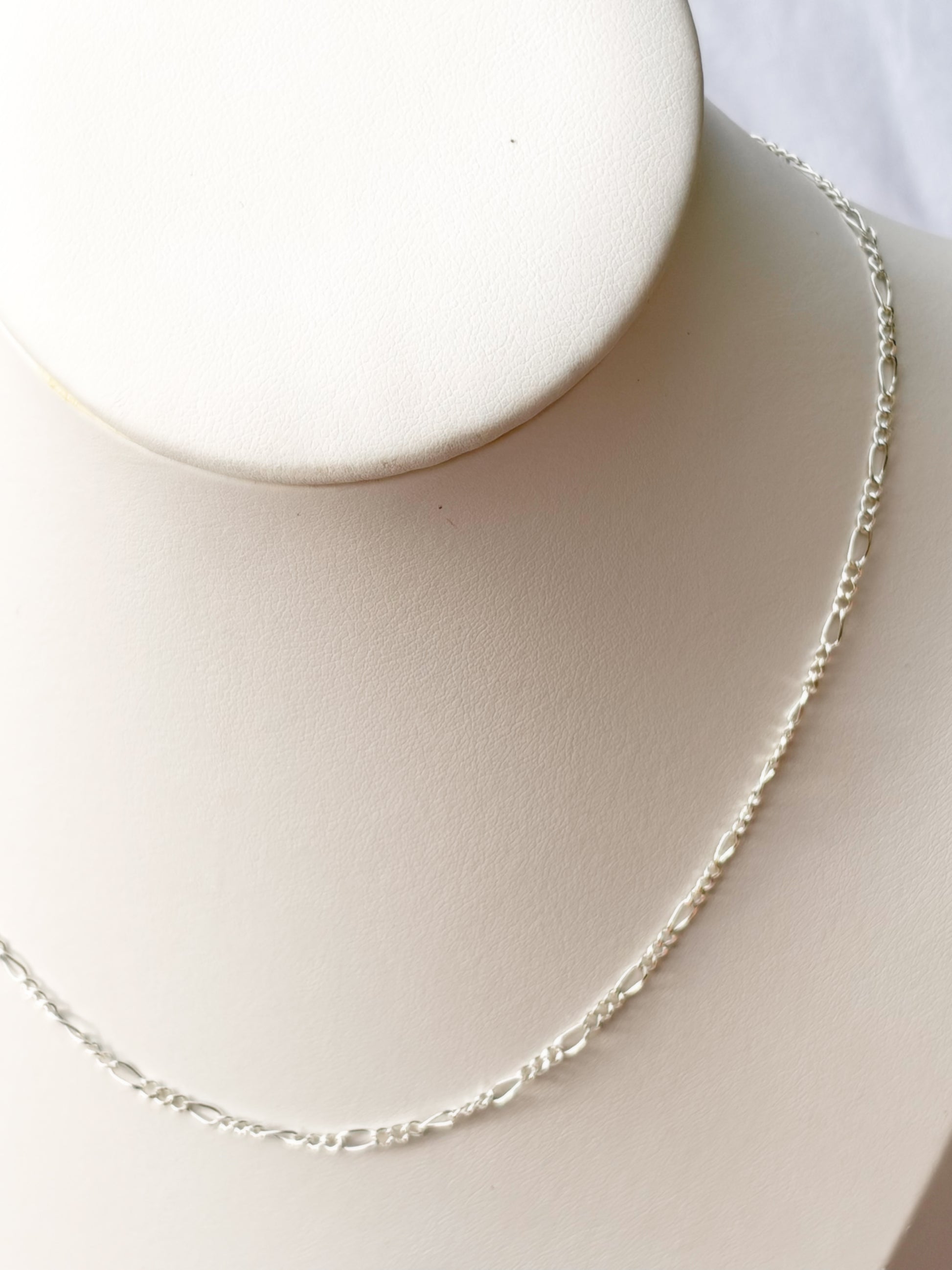 Close up of Figaro Silver chain Necklace on a white mannequin bust and background.