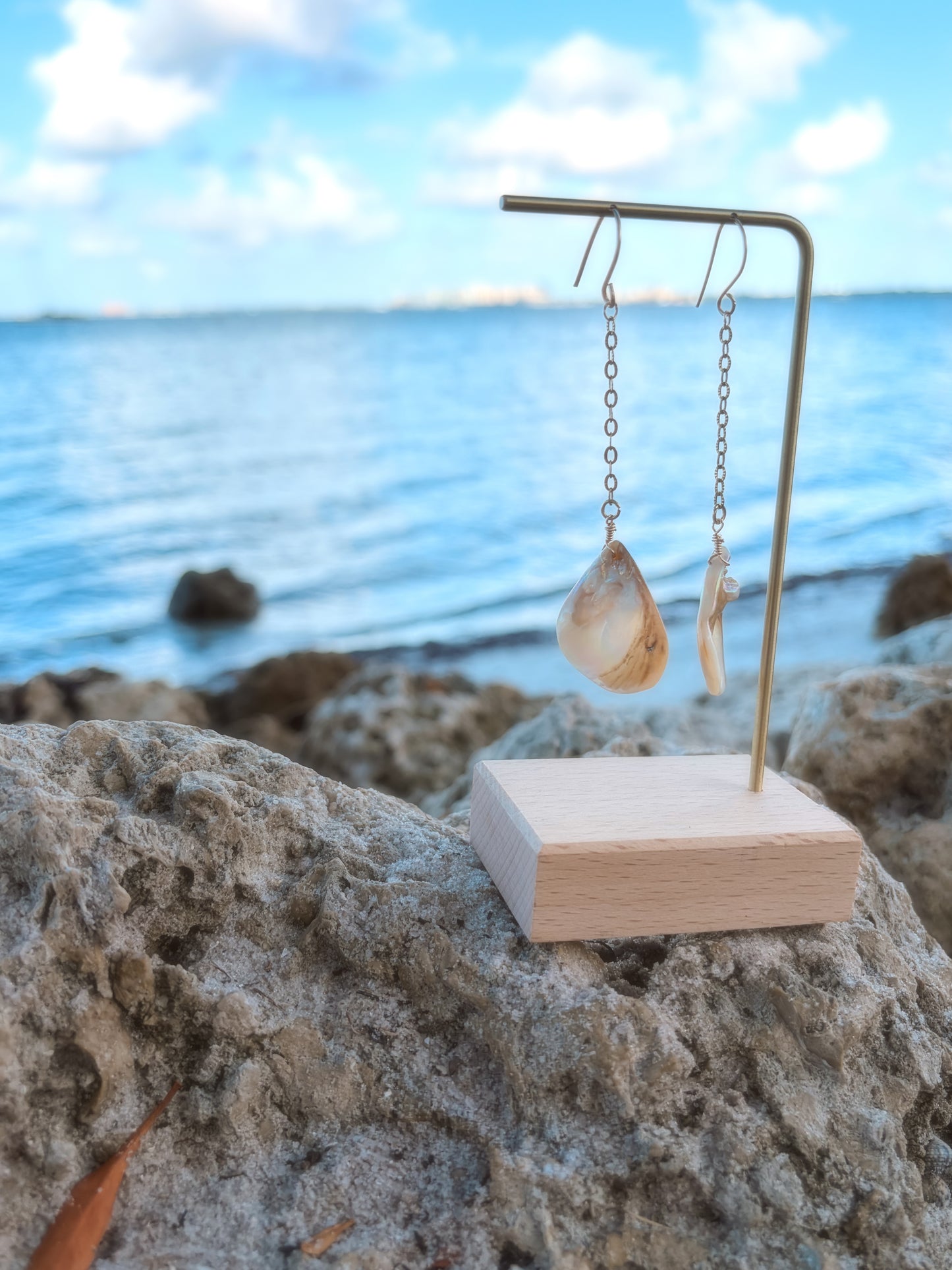 Beach close up of stainless steel dangly gold pearl/shell earrings.