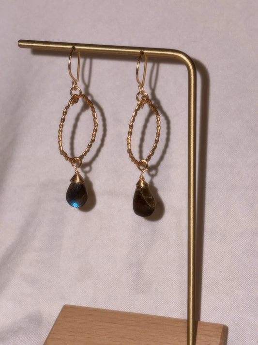 Gold earrings with Labradorite gemstones on a gold stand against a light background.